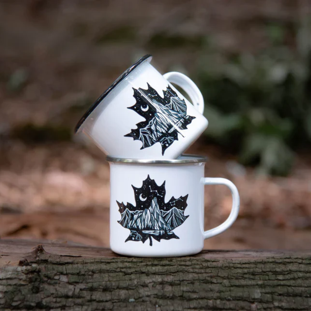 Two white mugs with black leaf designs on a wooden surface outdoors.