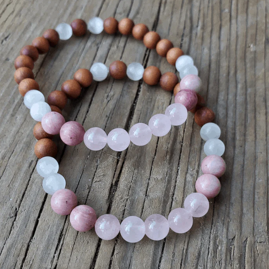 Two beaded bracelets on a wooden surface, one with brown, white, and pink beads, the other with pink and white beads.