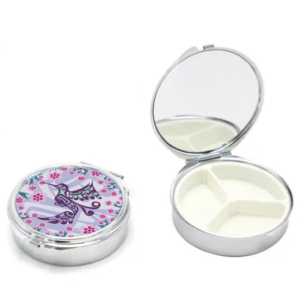 Compact pill organizer with a colorful hummingbird design on the lid, open to reveal white compartments.